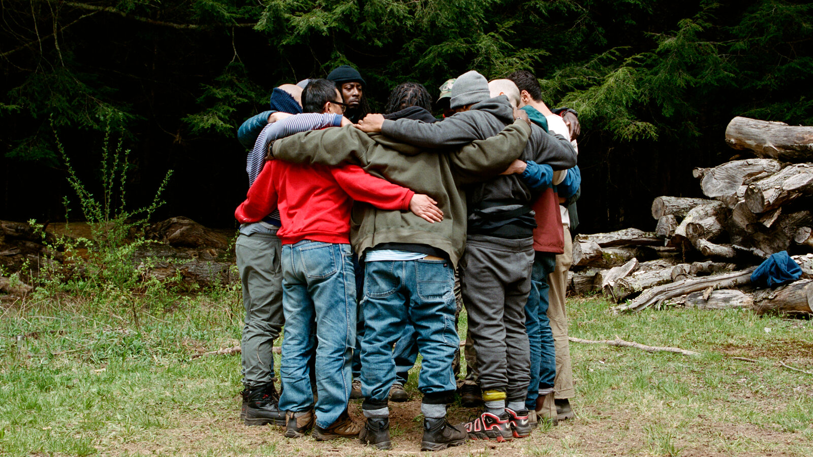 A diverse group of men in a close circle, arms around each other.