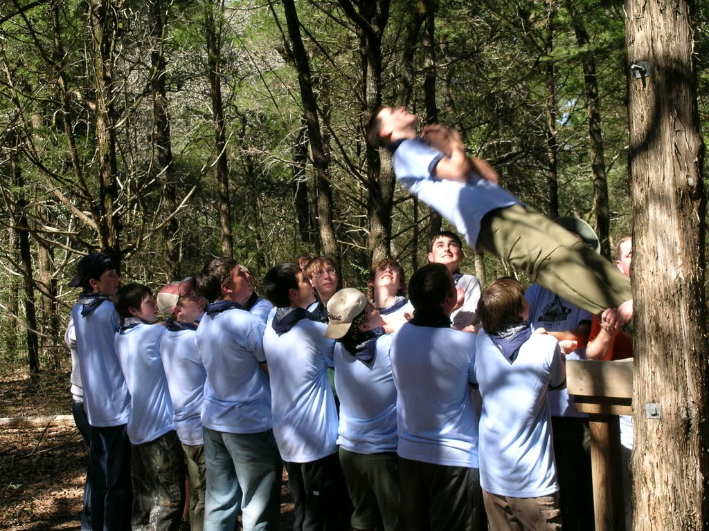 A group challenge exercise in the woods, one person lifted by the others.